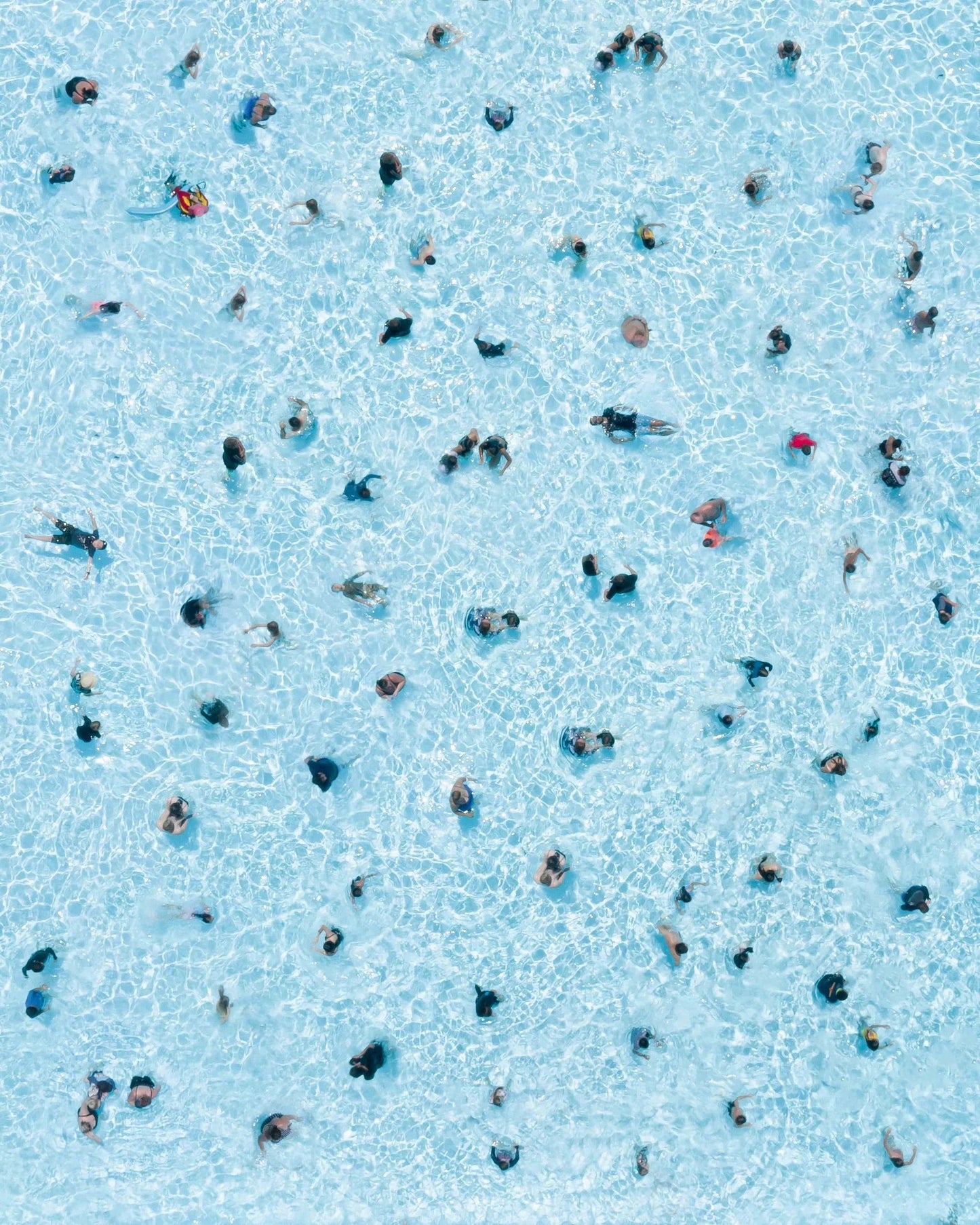 Top-down view of people swimming in a pool with clear blue water.