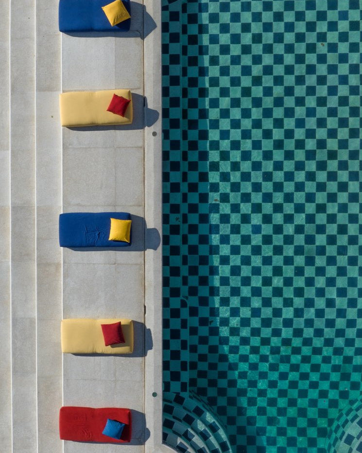 Colorful cushions on a concrete surface next to a pool with a checkered pattern.