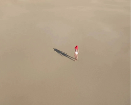 Person with a red hat standing on a sandy beach