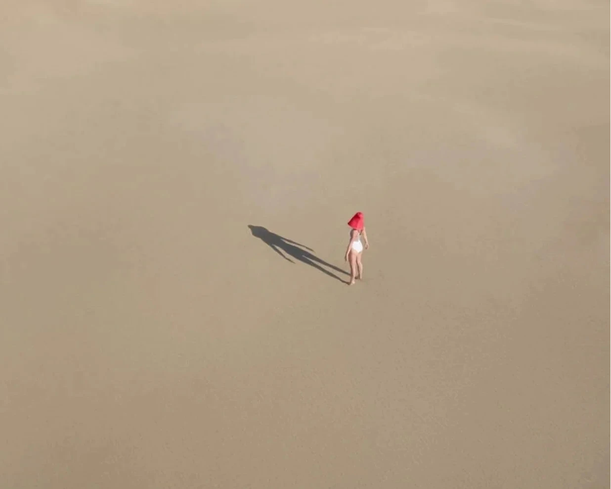 Person with a red hat standing on a sandy beach