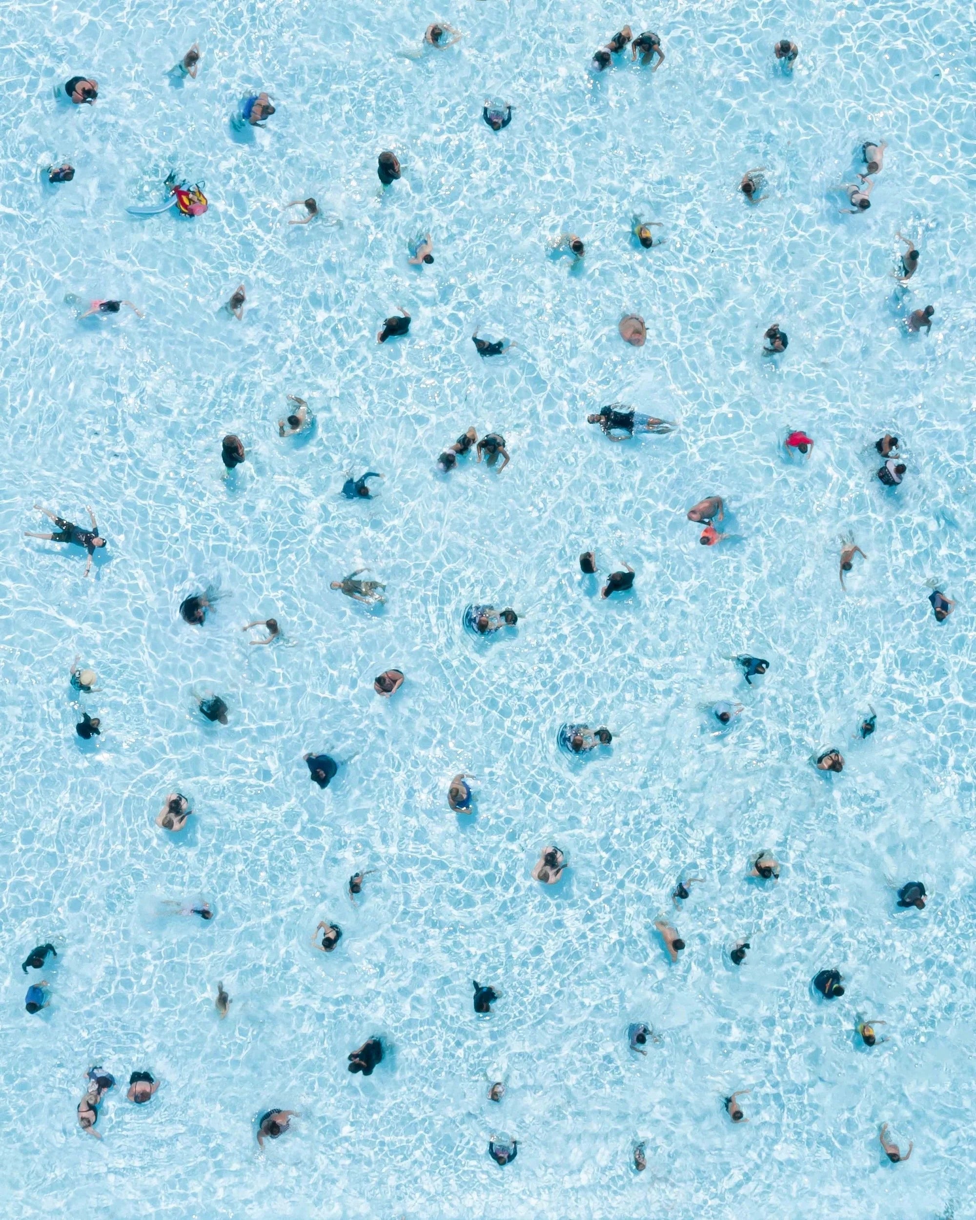 Top-down view of people swimming in a pool with clear blue water.