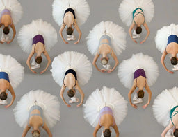 Multiple ballerinas in tutus performing a backbend against a gray background
